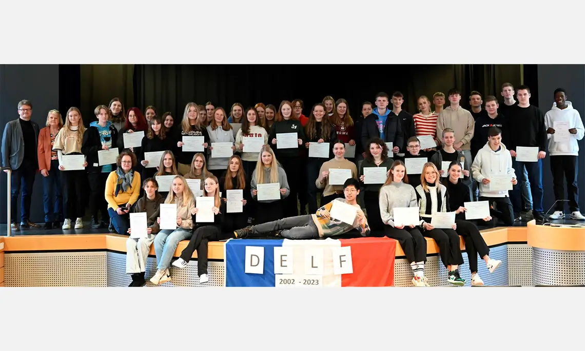 Die DELF-Absolventen des Jahres 2022 mit ihren Diplomen; links Schulleiter Hermann-Josef Rave sowie rechts daneben die betreuenden Lehrerinnen Andrea Sander und Martina Rensen (kniend). (Foto: Gymnasium Marianum Meppen)